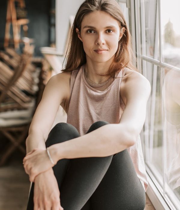 Woman in comfortable sportswear smiling peacefully in a bright, natural light setting.